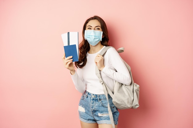 Covid and travelling concept happy woman traveller in medical mask holding passport and airplane tic...