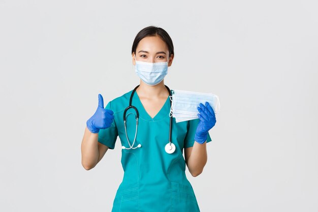 Covid19 coronavirus disease healthcare workers concept Smiling asian doctor nurse in scrubs and rubber gloves showing thumbsup and medical masks white background