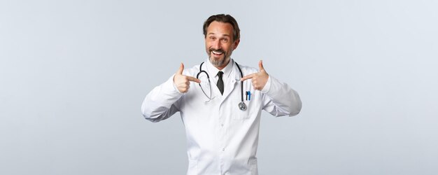 코비드19 코로나바이러스 발병 의료 종사자와 전염병 개념 흰색 코트를 입은 행복한 전문 남성 의사는 자신의 진료소나 자랑스러운 서비스를 홍보합니다