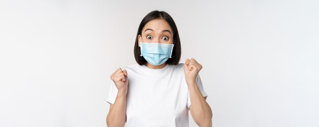 Covid19 concetto sanitario e medico donna asiatica entusiasta in maschera medica che balla e celebra la vittoria raggiungere l'obiettivo in piedi su sfondo bianco