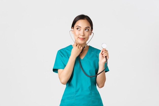 Covid19 healthcare workers and preventing virus concept Cute smiling asian female intern learn how listen lungs with stethscope doctor examine patient looking thoughtful upper left corner