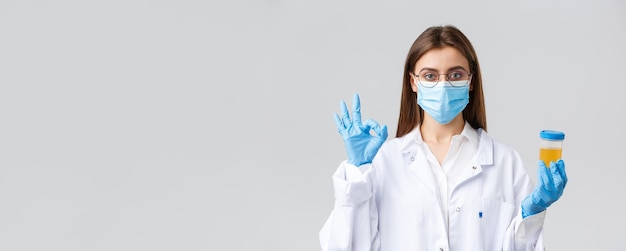 Covid19 medical research healthcare workers and quarantine concept professional doctor in scrubs medical mask and gloves holding patient urine sample and show okay sign approve making tests