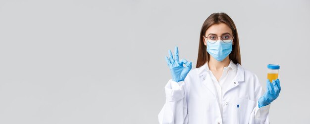 Covid19 의료 연구 의료 종사자 및 검역 개념 스크럽 의료 마스크와 장갑을 끼고 환자의 소변 샘플을 들고 있는 전문 의사가 검사를 승인한다는 표시를 보여줍니다.
