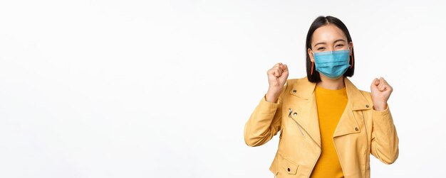 Covid19 and people concept Young asian woman in medical face mask dancing happy in casual clothes posing over white background