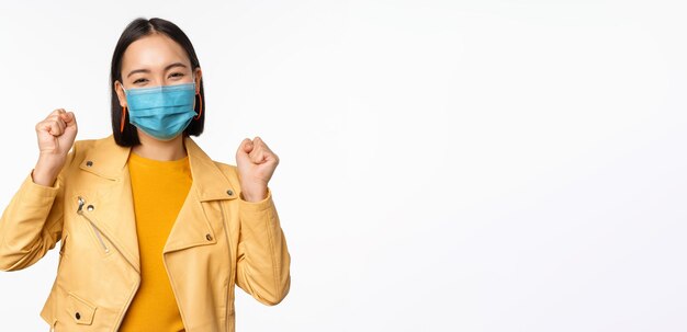 Covid19 and people concept Young asian woman in medical face mask dancing happy in casual clothes posing over white background