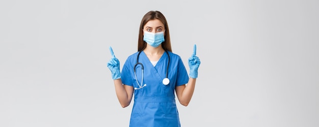 Covid19 preventing virus health healthcare workers concept Serious and confident female nurse in blue scrubs medical mask PPE pointing fingers up inform patients how prevent corona infection