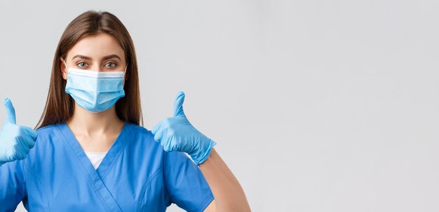Covid19ウイルスの健康医療従事者と検疫の概念を防ぐ青いスクラブで支援する女性看護師または医師のクローズアップ医療用マスクと手袋thumbsupの承認