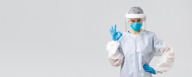 Covid19 예방 바이러스 건강 의료 종사자 및 검역 개념 PPE 보호복 인공 호흡기와 장갑을 끼고 있는 심각한 의사 전문 간호사가 괜찮은 표시를 보장합니다.