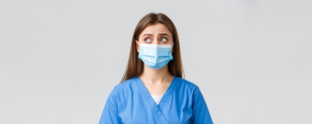 Covid19 예방 바이러스 건강 의료 종사자 및 검역 개념 회의적으로 고민하는 여성 간호사 또는 파란색 수술용 마스크를 쓴 의사는 왼쪽 상단 모서리가 불확실하거나 의아해 보입니다.