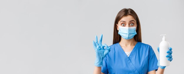 Covid19 preventing virus healthcare workers and quarantine concept Excited and enthusiastic female nurse or doctor in blue scrubs and medical mask recommend soap or hand sanitizer show okay