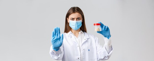 Covid19 예방 바이러스 의료 종사자 및 검역 개념 의료 마스크와 PPE를 착용한 심각한 우려 의사는 나쁜 약이나 항생제를 보여주는 이 약의 사용을 중단하라고 말합니다