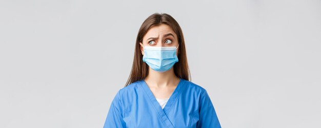 Covid19 preventing virus healthcare workers and quarantine concept Skeptical female nurse or doctor in blue scrubs medical mask raise one eyebrow intrigued and confused look upper left corner