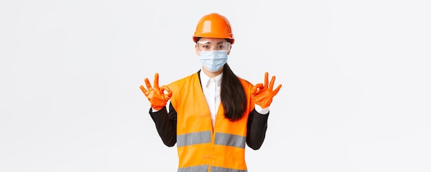 Протокол безопасности Covid19 при строительстве предприятия и предотвращении вирусной концепции Довольная азиатская женщина-инженер, промышленная женщина, маска для лица, показывающая хороший жест, хорошо сделанный, хвалящий хорошую работу