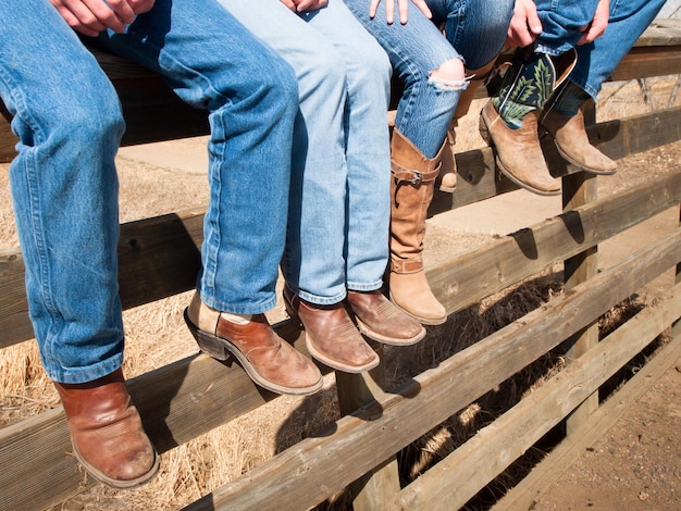 Cowboys and cowgirls sitting on wooden fence.