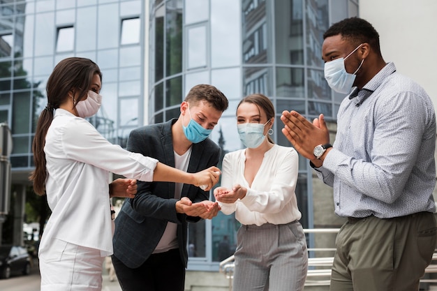 Coworkers disinfecting hands outdoors during pandemic while wearing masks