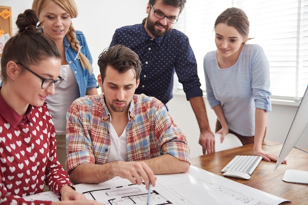 Coworkers at office with architecture plans and a computer