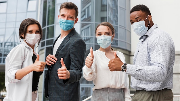 Coworkers outdoors during pandemic wearing masks and giving thumbs up