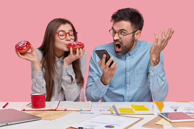 Coworkers sitting at desk with documents and gadgets