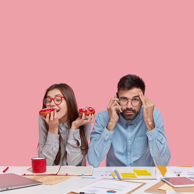 Coworkers sitting at desk with documents and gadgets