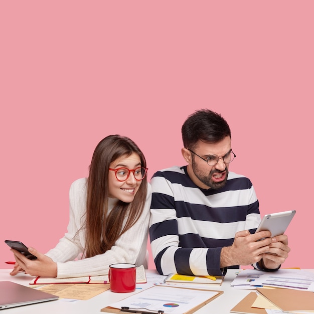 Coworkers sitting at desk with documents and gadgets