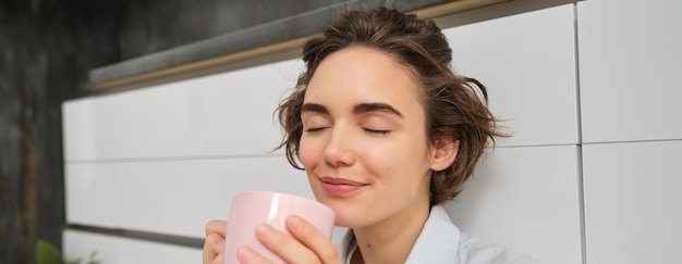 Coziness and home concept young woman enjoys her morning cup of coffee drinks fresh tea and smiles