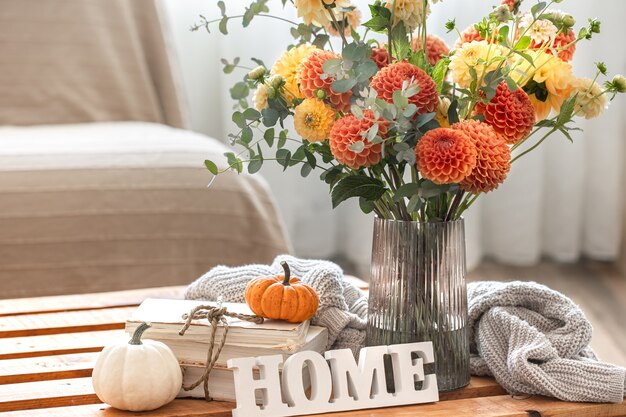 Cozy autumn composition with a bouquet of chrysanthemums in a vase, the decorative word home, pumpkins and a knitted element on a blurred background, copy space.