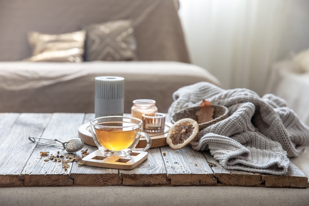 Free photo cozy autumn home composition with a cup of tea, candles and a knitted element on a blurred background of the room interior.