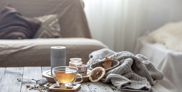 Cozy autumn home composition with a cup of tea, candles and a knitted element on a blurred background of the room interior.