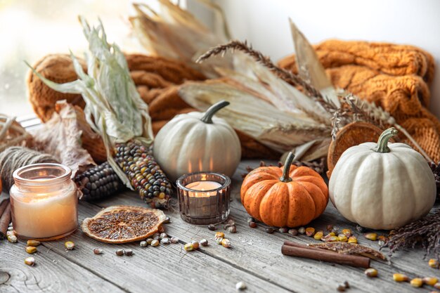 Cozy autumnal composition with candles, pumpkins, corn on a wooden surface in a rustic style.