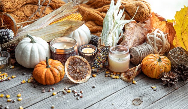 Cozy autumnal composition with candles, pumpkins, corn on a wooden surface in a rustic style.