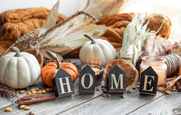 Free photo cozy autumnal composition with decorative word home, candles, pumpkins, corn on a wooden surface in a rustic style.