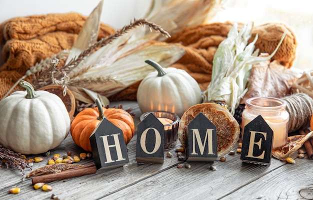 Cozy autumnal composition with decorative word home, candles, pumpkins, corn on a wooden surface in a rustic style.