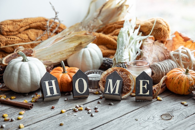 Cozy autumnal composition with decorative word home, candles, pumpkins, corn on a wooden surface in a rustic style.