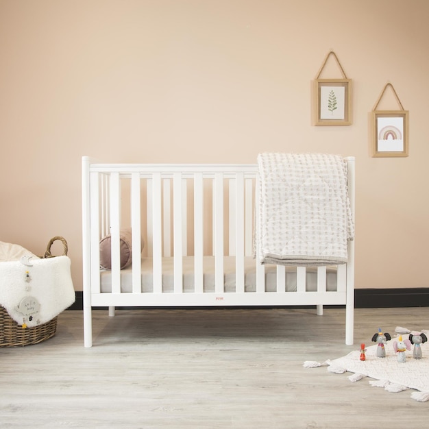 Cozy classic crib in a light baby room with toys on a soft carpet and a woven basket on the corner