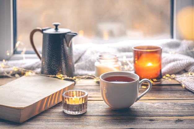 無料写真 窓のそばでお茶を飲み本とろうそくを照らす居心地の良いコンポジション