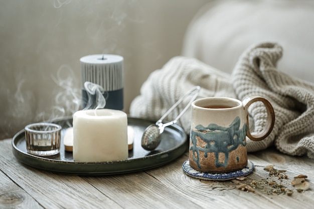 Cozy composition with a ceramic cup, candles and a knitted element on a blurred background.