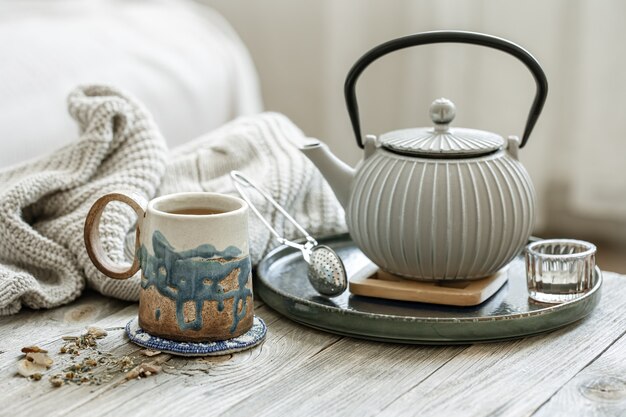 Cozy composition with a ceramic cup, a teapot and a knitted element on a blurred background.