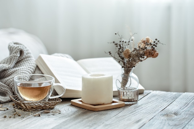 A cozy composition with a cup of tea, a book and decor details in the interior of the room on a blurred background.
