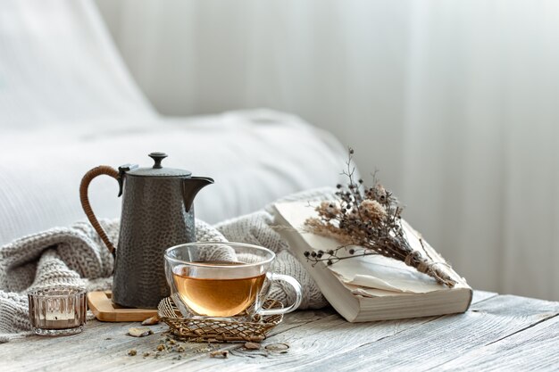 Cozy composition with a cup of tea and a book in the interior of the room on a blurred background.