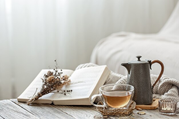 Cozy composition with a cup of tea and a book in the interior of the room on a blurred background.
