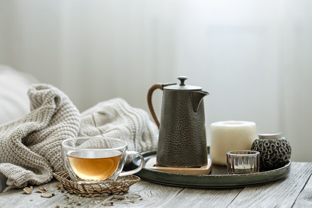 Уютная композиция с чашкой чая, свечой в интерьере комнаты на размытом фоне.