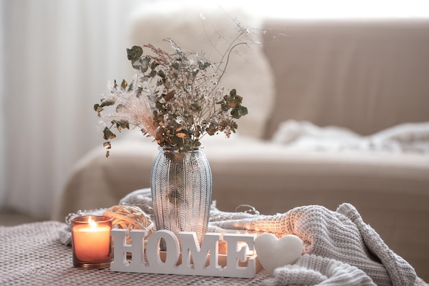 Cozy composition with decorative word home candles and vase with dried flowers