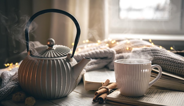 Foto gratuita composizione accogliente con una teiera una tazza e un libro su uno sfondo sfocato