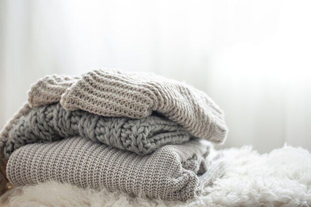 Cozy gray knitted sweaters stacked on blurred background, copy space.