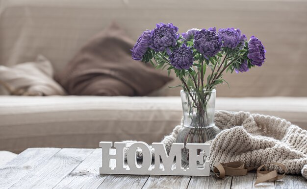 Cozy home composition with a bouquet of blue chrysanthemums in a glass vase and the decorative word home.