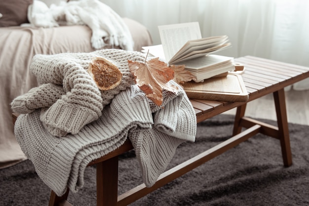 Free photo a cozy home composition with a knitted sweater, a book and leaves in the interior of the room.