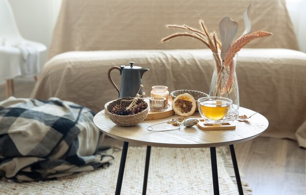 Cozy home still life with a cup of tea, pumpkins, candles and details of autumn decor on a table on a blurred background.