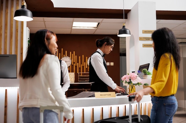 Free photo cozy hotel reception with two female guests waiting for concierge to finalize booking procedure. relaxed customers holding baggages getting ready to check in at lavish resort