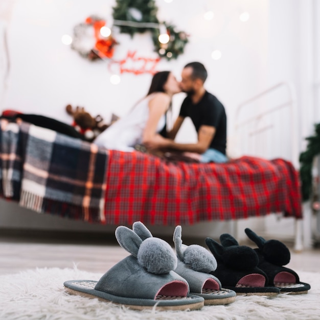 Cozy house shoes on floor near kissing couple on bed