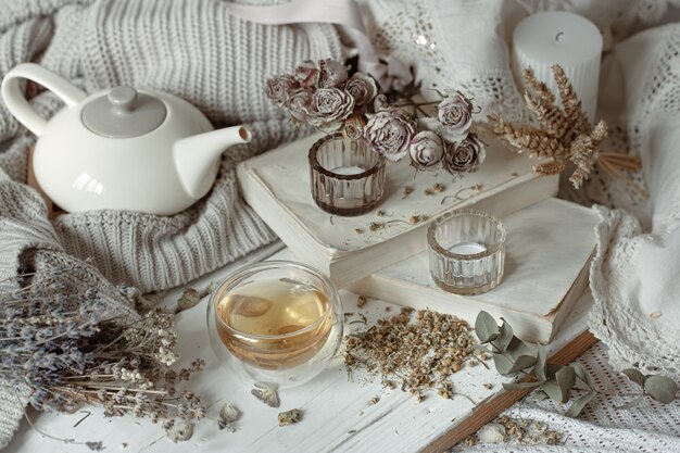 Cozy light still life with candles, a cup of tea, a teapot and dry herbs.